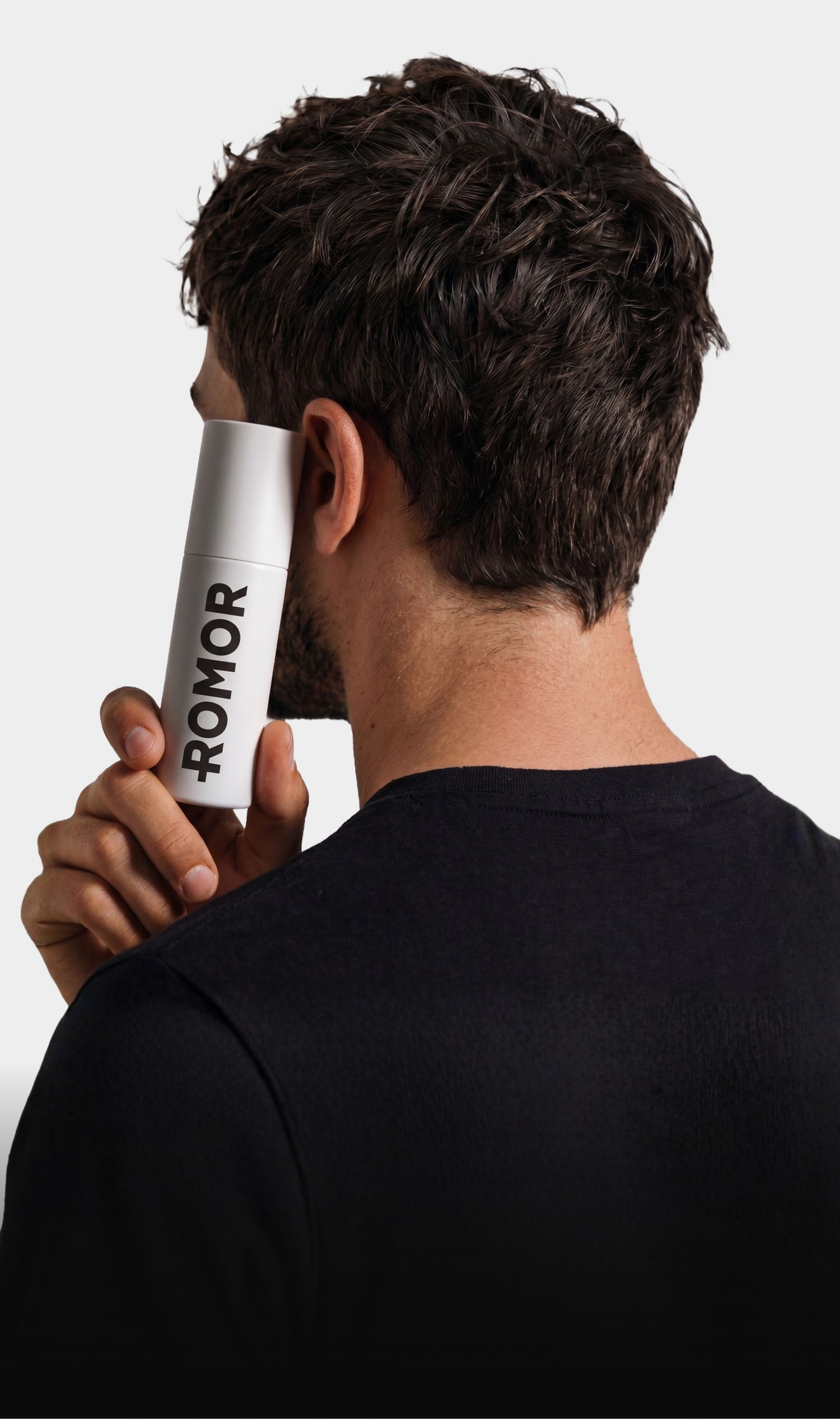 A man shown from behind holding a white cylindrical bottle with the brand name 'ROMOR' printed vertically in black, against a plain light gray background.